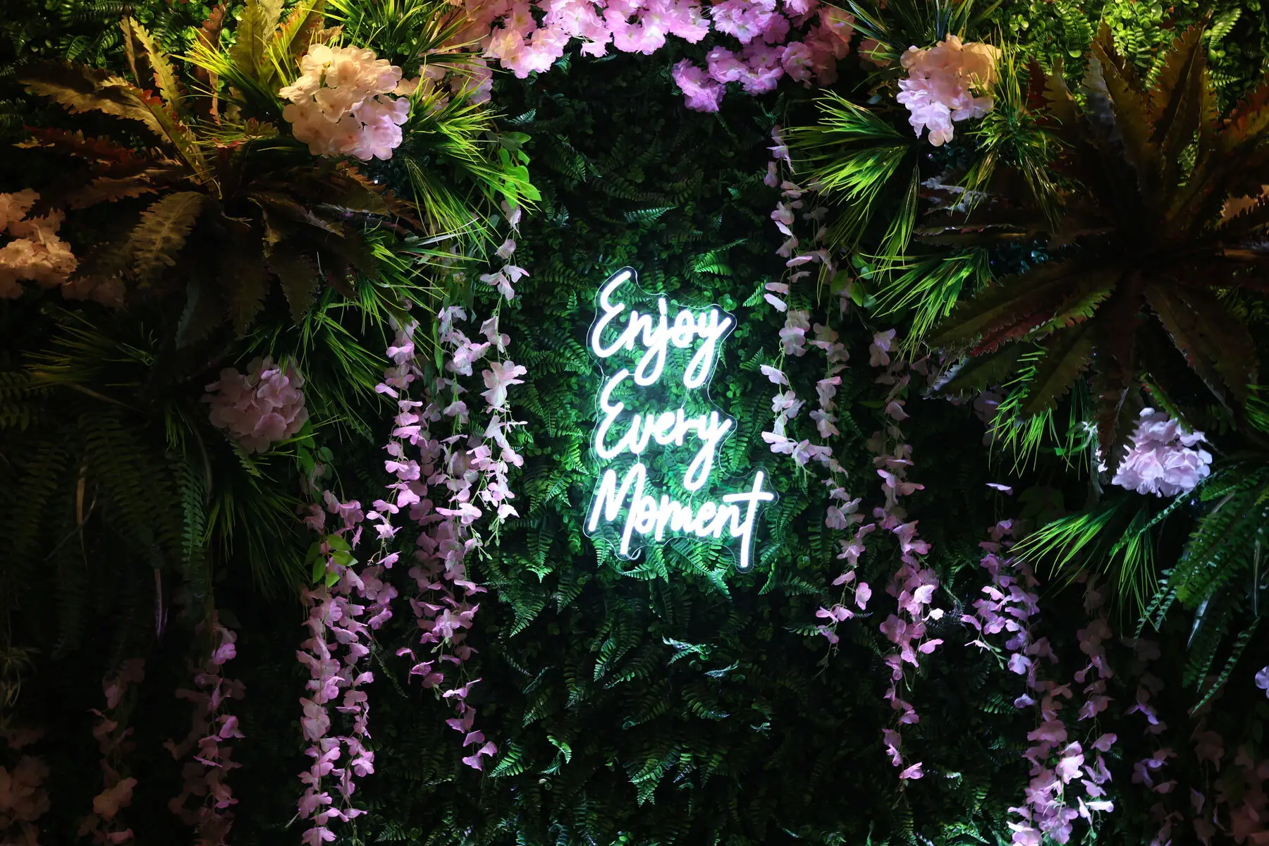 Enjoy Every Moment neon sign in the flower wall